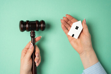 The female hand holding the wooden house and the judge's hammer. Real estate court decisions. Property inheritance litigation. Establishment of ownership.