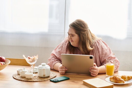 Young woman with Down syndrome enjoying a cozy moment at home with a tablet and breakfast