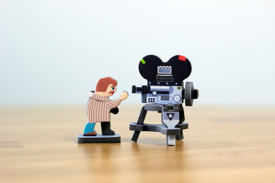 small paper-made figurine of a DOP / director of photography / director / cameraman looking into a big film camera, shooting concept, cinema, directing concept, filmmaking