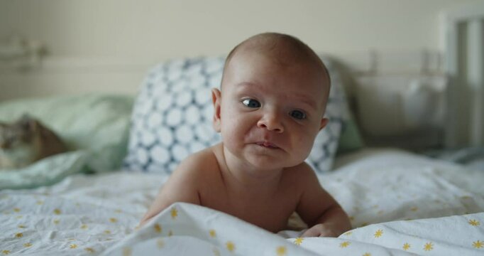 Little newborn child trying to hold his head up lying on a bed. The baby puts all his strength into lifting his head and crawling.