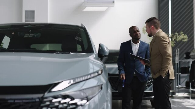 A car dealer in a modern car dealership advises an African-American customer on buying or leasing a new car. The concept of an expensive purchase or lease of a modern car.
