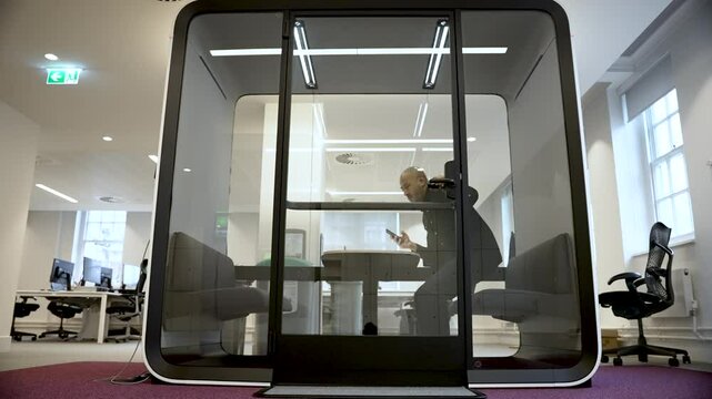South asian businessman entering a soundproof booth in a modern office to take a private phone call, holding his smartphone