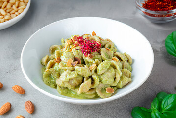 Orecchiette pasta with broccoli pesto in a white bowl, garnished with almonds and saffron....