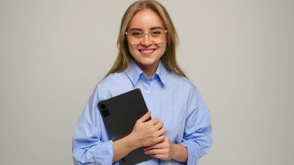 A smiling woman stands in a light studio, holding a tablet close to her.
