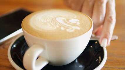 Latte with delicate foam served on wooden table beside smartphone in cozy cafe Latte adds warmth to coffee pause Latte art enhances relaxing moment ideal for modern lifestyle and digital detox 