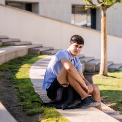 Teenage boy student 17 years old with a backpack sits on the wooden steps outside the college