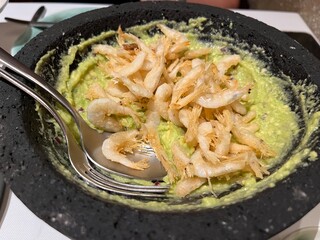 Delicious guacamole with fried shrimps served in stone bowl with cutlery