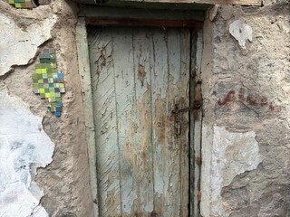 Very old door with peeling light green and light blue paint with rusty lock and latch on the door in an old stone room