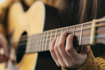 Fototapeta premium Close up of woman playing acoustic guitar, focusing on her hand on fretboard, creating warm and artistic mood
