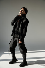Stylish young asian man confidently posing in trendy black attire against minimalist backdrop
