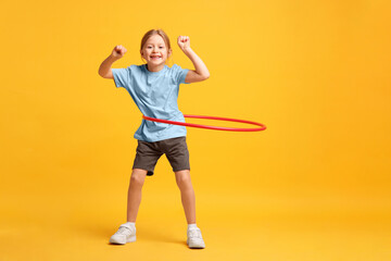 Cute little girl exercising with hula hoop on orange background