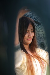 A serene Pakistani girl glances downward with a tender smile, surrounded by intricate patterns dupatta and soft sunlight, exuding grace and charm.