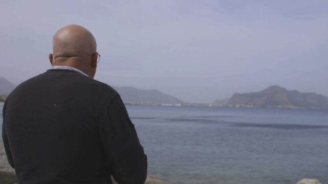Uomo di spalle, beve birra su una spiaggia mentre guarda il mare.