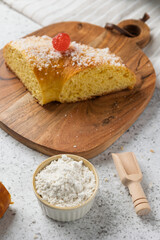 Slice of roscón de reyes with candied fruit on wooden board, flour in bowl and wooden scoop