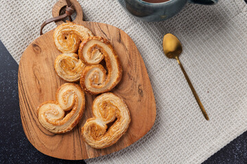 Delicious palmier pastries resting on wooden board with cup of coffee and golden spoon