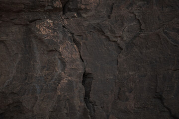 A textured stone background with chiaroscuro lighting, highlighting a brutal, monolithic rock formation. Cracks and fragments showcase its geological power, perfect for design or science-themed