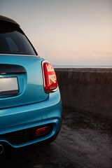 Naklejka premium Blue compact car at dusk. Rear part of hatchback in parking lot, close-up view of the right rear tail light. 
