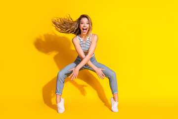 Excited young woman posing against a vibrant yellow background with a joyful expression and...