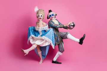 Young couple in festive baroque costumes having fun at a carnival party, dancing joyfully against a...