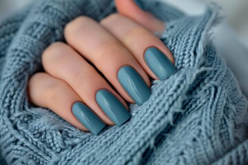 Perfectly manicured teal nails wrapped in a cozy soft knitted fabric in a serene indoor setting