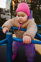 Child Enjoys Spinning on Playground Equipment in Vibrant Winter Attire During Sunny Afternoon