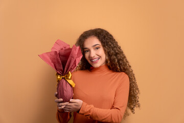 cheerful teen girl celebrating easter egg gift in beige studio background. holiday, easter, celebration concept.