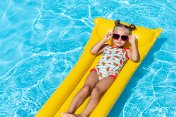 Cute little girl lying on inflatable mattress in swimming pool with blue water on warm day on tropical vacations. Summertime activities concept. advertising of tour operators and all-inclusive hotels