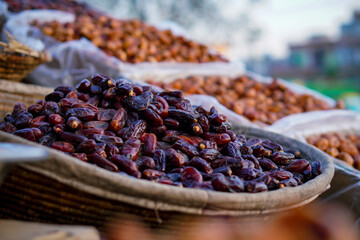 A close-up of glossy dark dates displayed in a woven basket at an outdoor market.