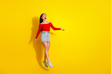 Young woman in vibrant outfit expressing excitement with a cheerful jump against a vivid yellow background
