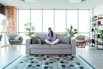 Charming woman relaxing on a cozy sofa in a modern living room interior with large windows and...