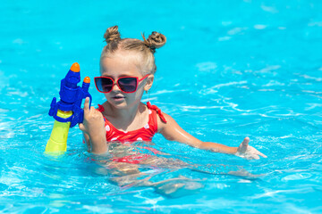 Laughing child playing with water gun in outdoor swimming pool on summer day. Pool toys and water fun for family with children. Summer vacation with kids. Active outdoor sport for preschooler.