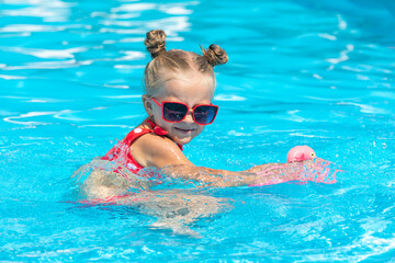 Little girl having fun on vacation at the hotel pool. Colorful vacation concept. Summer outdoor activity during family vacation in tropical resort. Beach and water toys. Sun protection.