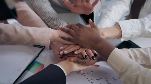 African American Japanese Hispanic multiethnic business women females team girls coworkers businesswomen hands arms folded in unity gesture cooperation teamwork partnership documents table at office