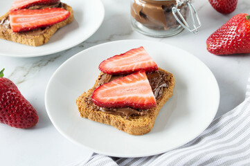 Fresh toasts with chocolate paste and berries serve for delicious breakfast. Spreading sweet chocolate cream onto toast on table.