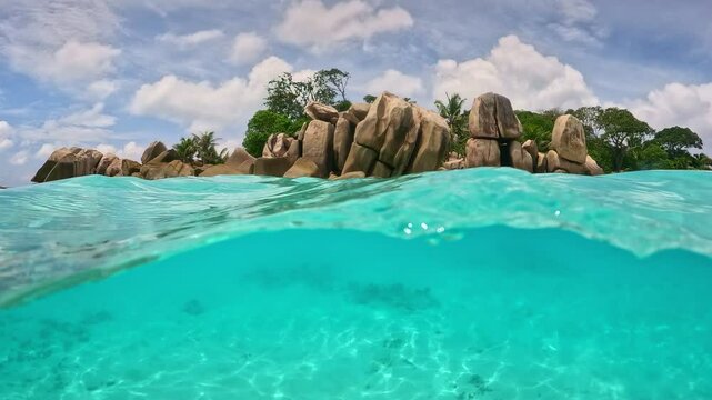 Half underwater slow motion shot of turquoise water, rocks and trees on tropical island in Seychelles. Stunning underwater view of crystal clear water and rocky shoreline in tropical paradise
