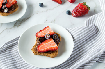 Fresh toasts with chocolate paste and berries serve for delicious breakfast. Spreading sweet chocolate cream onto toast on table.
