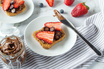 Fresh toasts with chocolate paste and berries serve for delicious breakfast. Spreading sweet...
