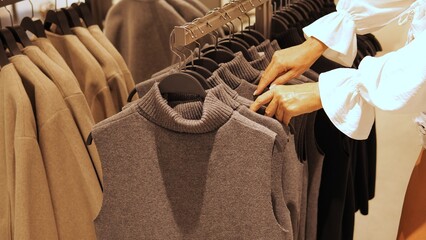 Woman carefully selects sweater evaluating clothing styles and quality Shopping for cozy clothing highlights fashion preferences Clothing choice reflects personal style comfort and seasonal trends