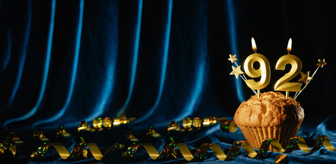 Number 92 gold celebration candle and small stars in sweet cupcake on bright blue velvet background. Concept of celebrating birthday, anniversary. Banner.