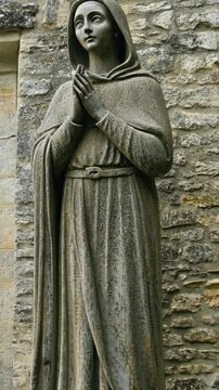 Statue of a praying figure near an ancient stone wall in a tranquil garden setting