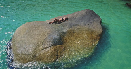A person rests peacefully on a large rock surrounded by pristine turquoise water. The scene captures a serene moment, likely enjoyed during a warm, sunny day.