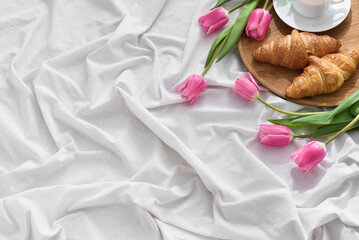 Delighting a mother on Mother's Day with a lovely breakfast in bed. Soft white linens hold fresh tulips and delicious croissants alongside a steaming cup of coffee.