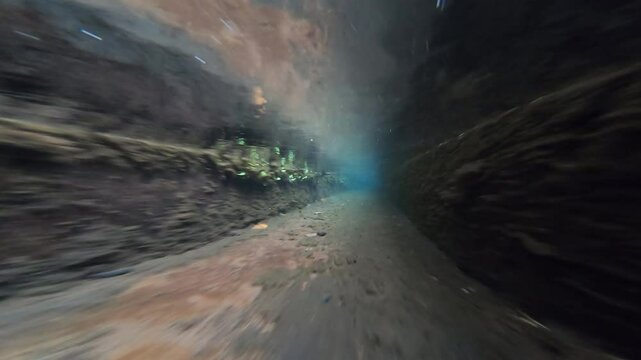 Sunlight pierces through the underwater currents of a levada tunnel, illuminating swirling bubbles and moss-covered rock walls.