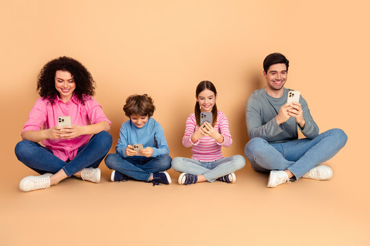 Happy family using smartphones together while seated on a beige background in casual attire, showcasing modern bonding