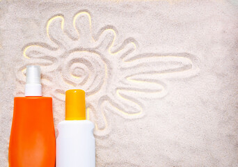 Two protection sunscreen (sun cream) bottles on sand. The sun drawing on the sand background. Sun tan, summer skin care. UV protection, photoaging, skin health concept. Copy space. Empty plac.