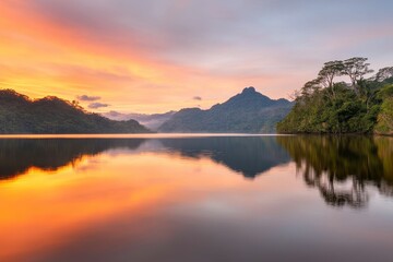 Fototapeta premium A tranquil lake reflects vibrant sunset colors, surrounded by lush mountains and trees, creating a serene and picturesque landscape.
