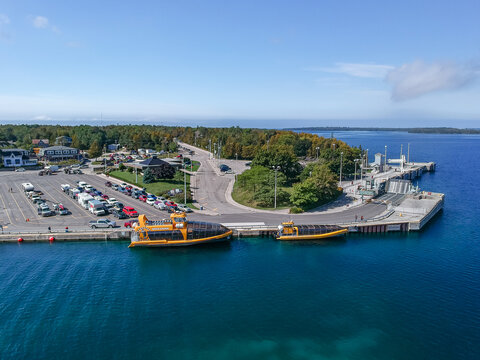 Aerial drone photo of the marina with clear emerald water with glass bottom tour boats, tourist parking lots, restaurants and hotel in Tobermory - a tourist town in Bruce Peninsula. Ontario, Canada.