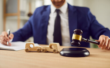 Close up shot of a lawyer holds a gavel beside two toy cars, illustrating legal proceedings...