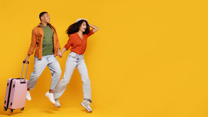 Ready for vacation. Happy Latin couple running with suitcase over yellow background, spouses...
