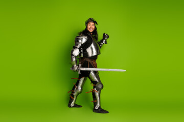 Young man in medieval knight armor with sword posing on a bright green background